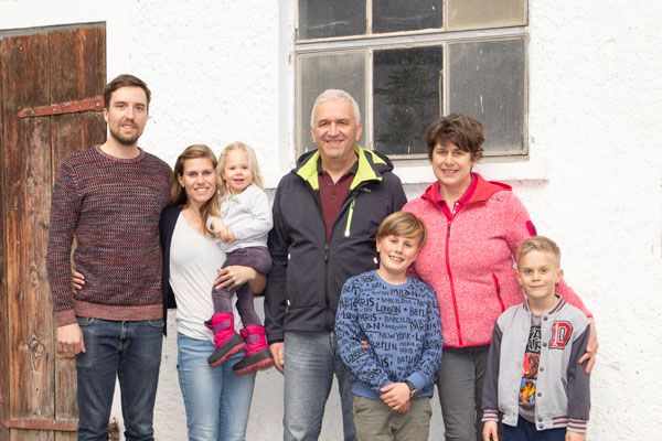 Drei Generationen einer Familie stehen lächelnd vor einem weißen Haus mit Fenster und Holztür
