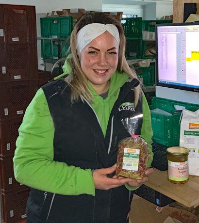Frau in grünem Pullover und schwarzer Weste zeigt ein Produkt in Verpackung in Lagerraum