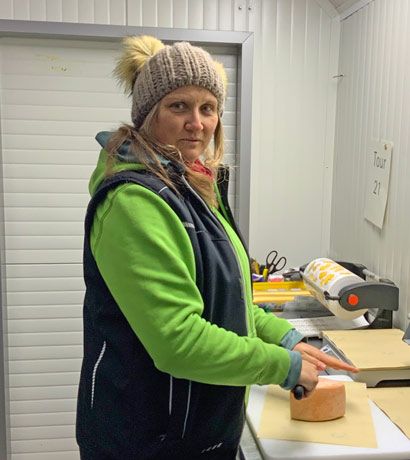 Frau mit Wintermütze schneidet Käse in einer Küche mit Verpackungsmaschine
