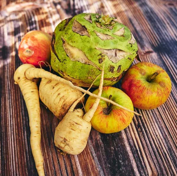 Verschiedene frische Äpfel und Wurzelgemüse auf hölzernem Untergrund arrangiert