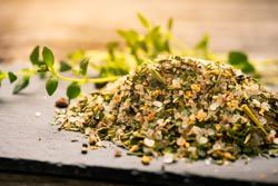 Ein Haufen bunter, getrockneter Kräuter und Gewürze auf einer schwarzen Oberfläche mit frischem Grün im Hintergrund