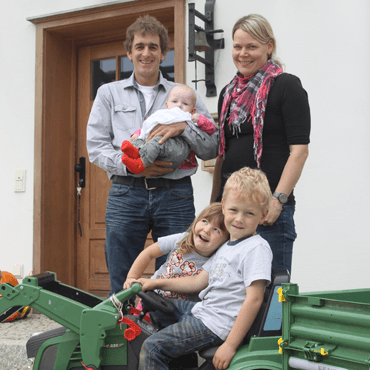 Glückliche Familie mit Eltern und drei Kindern vor Haustür mit Spielzeugtraktor