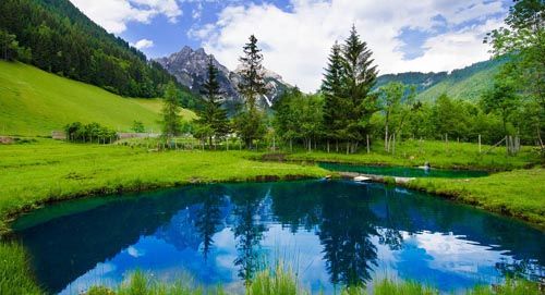 Kleiner blauer Bergsee mit Spiegelung von Tannen und Bergen unter bewölktem Himmel