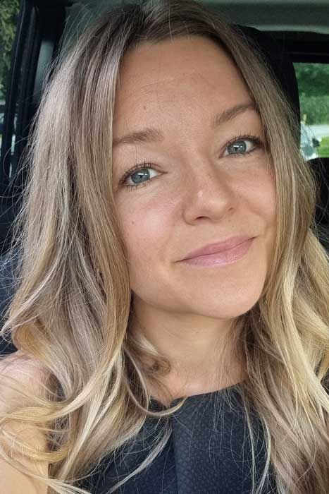 Lächelnde Frau mit langen blonden Haaren sitzt in einem Auto
