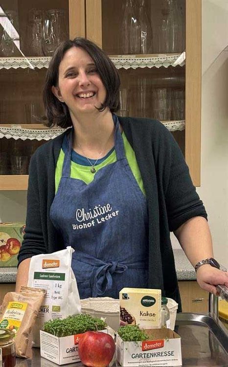 Frau in Schürze steht lächelnd in Küche mit Bioprodukten und Gartenkresse vor ihr