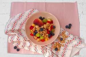 Schale mit Müsli, frischen Beeren und Trauben auf weißer Stoffserviette mit roten Mustern