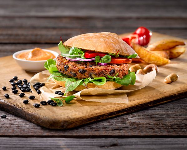 Veganer Burger mit schwarzen Bohnen, Salat und Tomaten auf Holzbrett mit Soße und Kartoffelecken